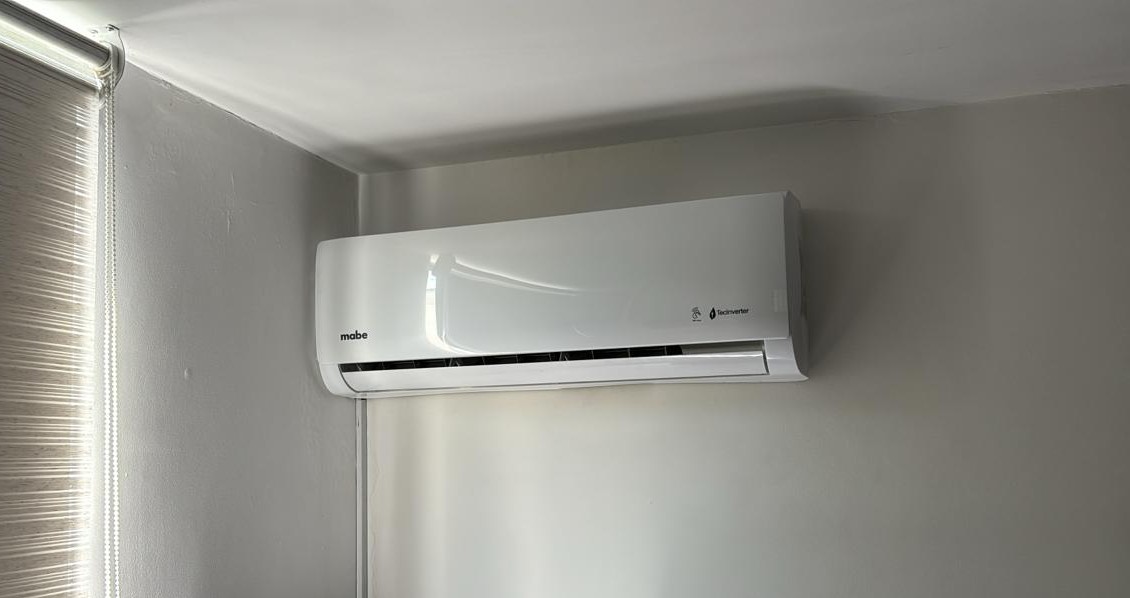 Modern residential home with large windows and a well-maintained garden, featuring an outdoor air conditioning unit installed near the house. The environment is peaceful and inviting, with green plants and a clear sky. No visible text in the image.